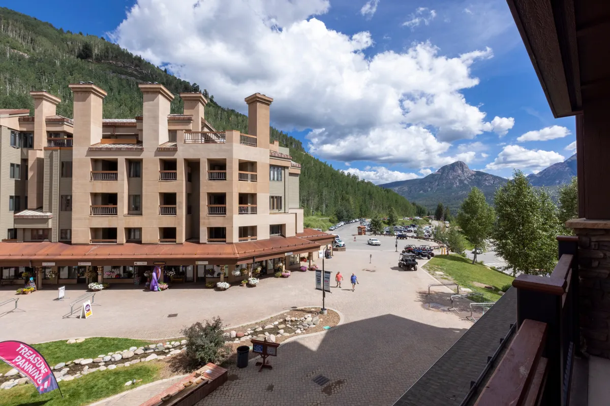 An exterior shot featuring the building facade of Purgatory Lodge, with people casually strolling, outdoor seating, and shops visible. The vibrant mix of activity highlights easy access to village amenities, boutiques, and dining, all set against a stunning mountain backdrop.