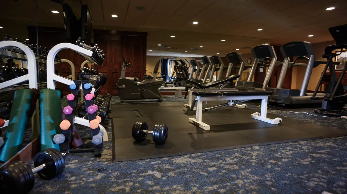 A well-equipped fitness center featuring dumbbells, treadmills, a weight bench, and various exercise machines. The space is lit to feel motivational and dynamic, inviting guests to maintain their fitness routines during their stay.