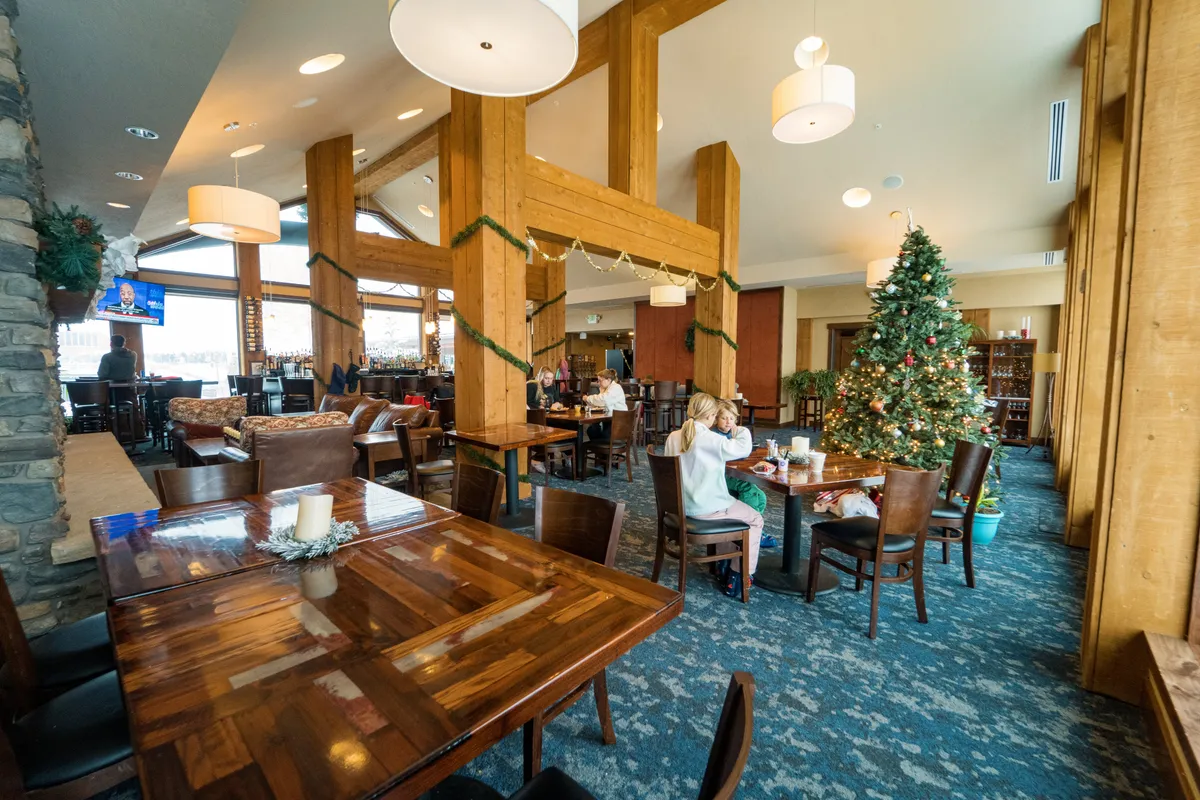 A lively, warmly decorated interior common area with large wooden beams, a festive Christmas tree, and ample seating. The space is clearly designed for gatherings, celebrations, and family bonding, evoking moments of lively group activity and memorable holidays.