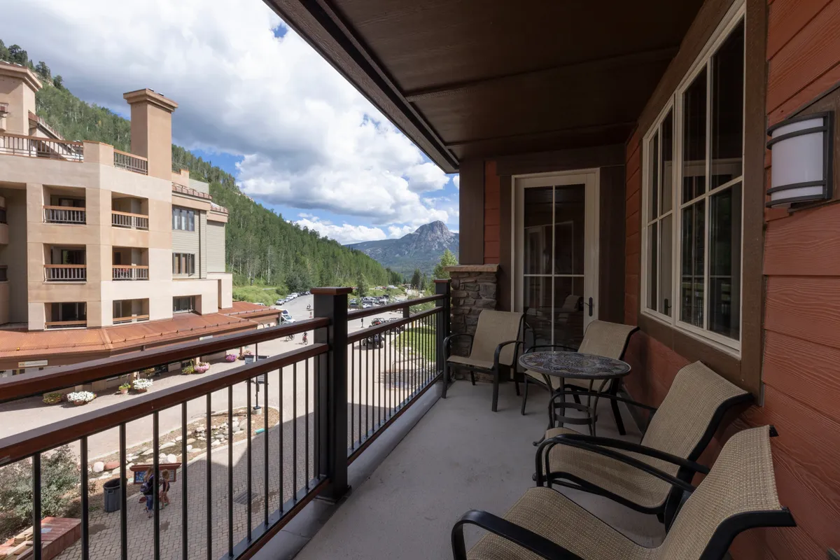 An exterior shot of a private balcony with comfortable seating, offering a panoramic view of the mountains and capturing architectural elements of the building. The serene mood suggests a tranquil setting for morning coffee or evening toasts.