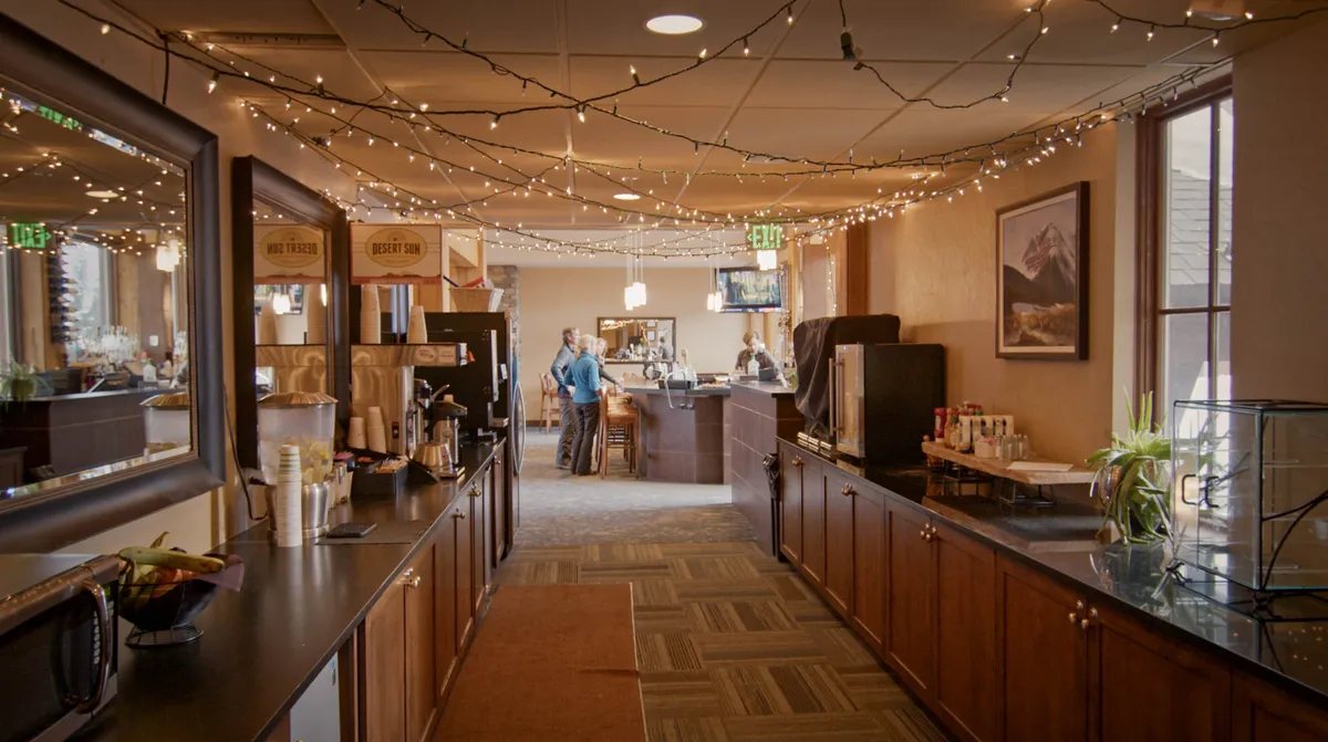 A cozy lounge area featuring a coffee station, bar, decorative lights, and framed landscape art. The space is arranged for relaxation and socializing, perfect for unwinding solo or with friends.