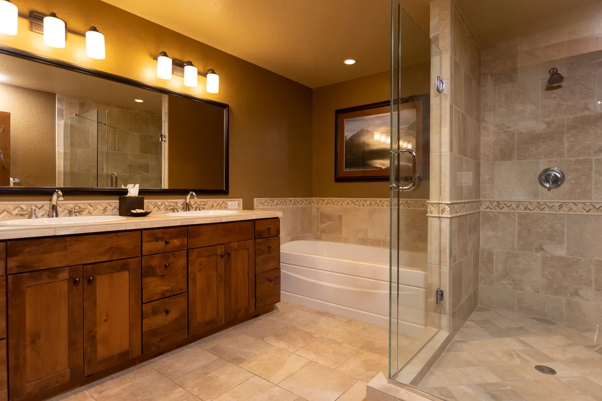 A serene bathroom featuring a double sink vanity, a large framed mirror, a bathtub, a glass shower enclosure, and framed artwork. The layout offers both functionality and a spa-like retreat.