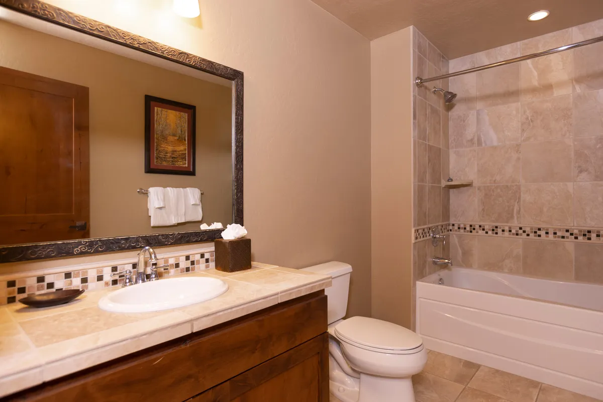 A tranquil bathroom space with a vanity, sink, mirror, bathtub, and a tiled shower area, inviting guests to enjoy both relaxing soaks and refreshing showers after a day outdoors.