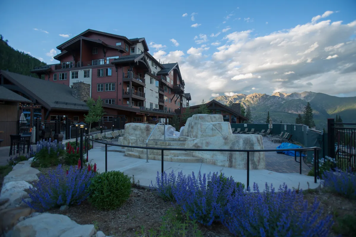 A beautifully landscaped garden space in front of the property, featuring a rock fountain, vibrant flower beds, and the mountain backdrop. Guests can be imagined relaxing by the fountain or socializing in the open-air garden, reinforcing the sense of community and leisure.