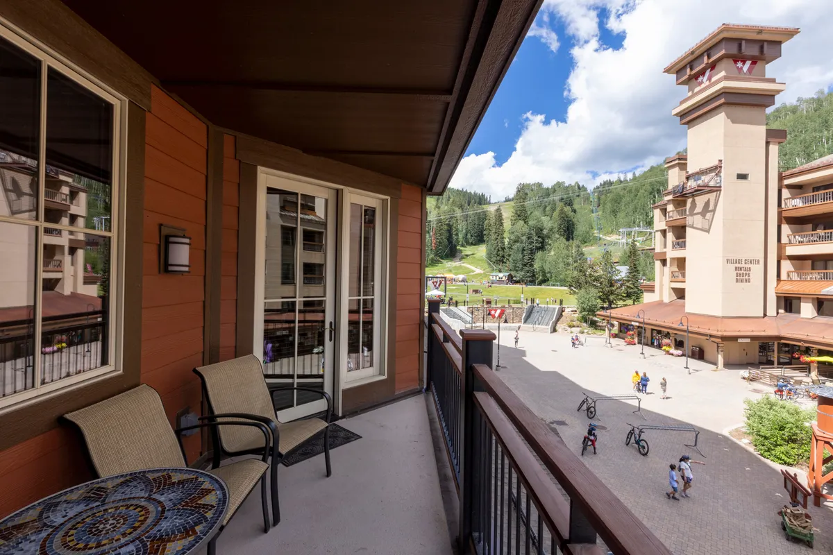 Taken from a balcony, this exterior shot showcases comfortable seating with a sweeping view of the mountains and an outdoor plaza below. The vibrant atmosphere hints at après-ski relaxation, people-watching, and enjoying the fresh air after a day on the slopes.